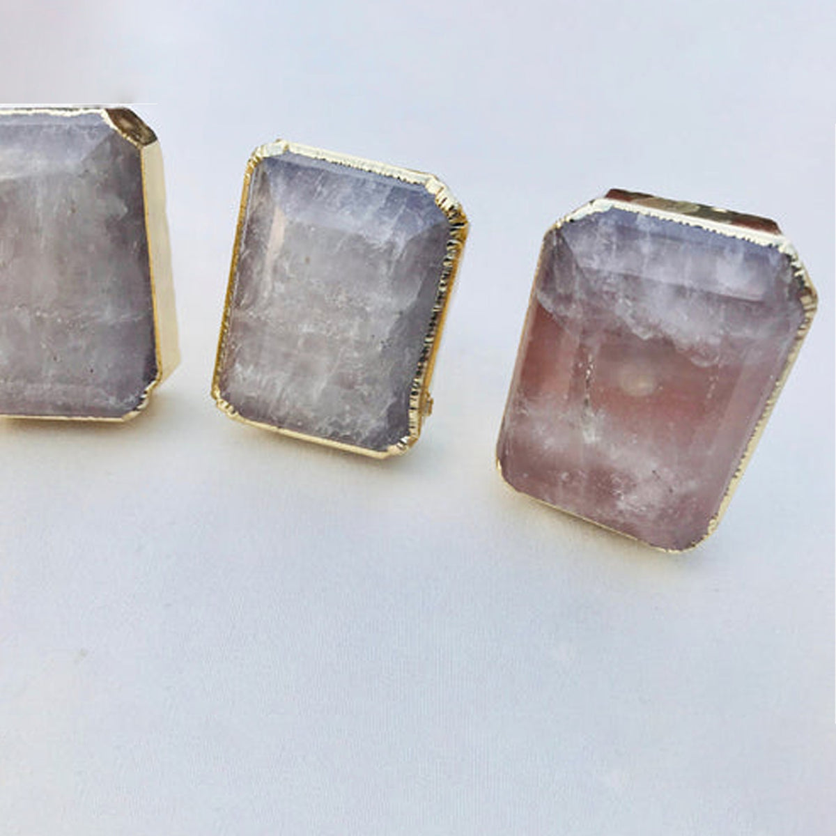 Close-up of emerald-cut quartz knobs, milky with a pink tint at the base, in gold bezels