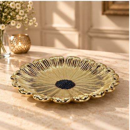 Gold flower dish with a dark beaded center on a marble counter, seen at an angle