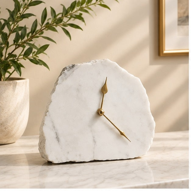 White marble desk clock on a marble counter beside a plant