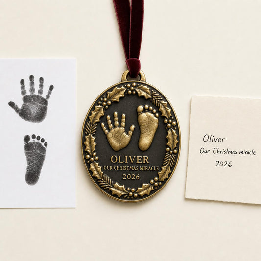 An antique brass oval baby ornament framed in holly, with a raised handprint and footprint