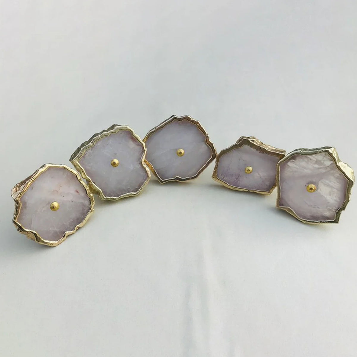 Five pale pink rose quartz slice knobs laid in a curve, each with a gold edge and center pin