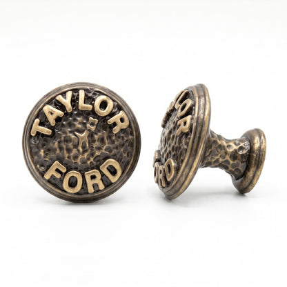 Two antique brass name knobs reading TAYLOR FORD on a hammered face, one turned to show its stem