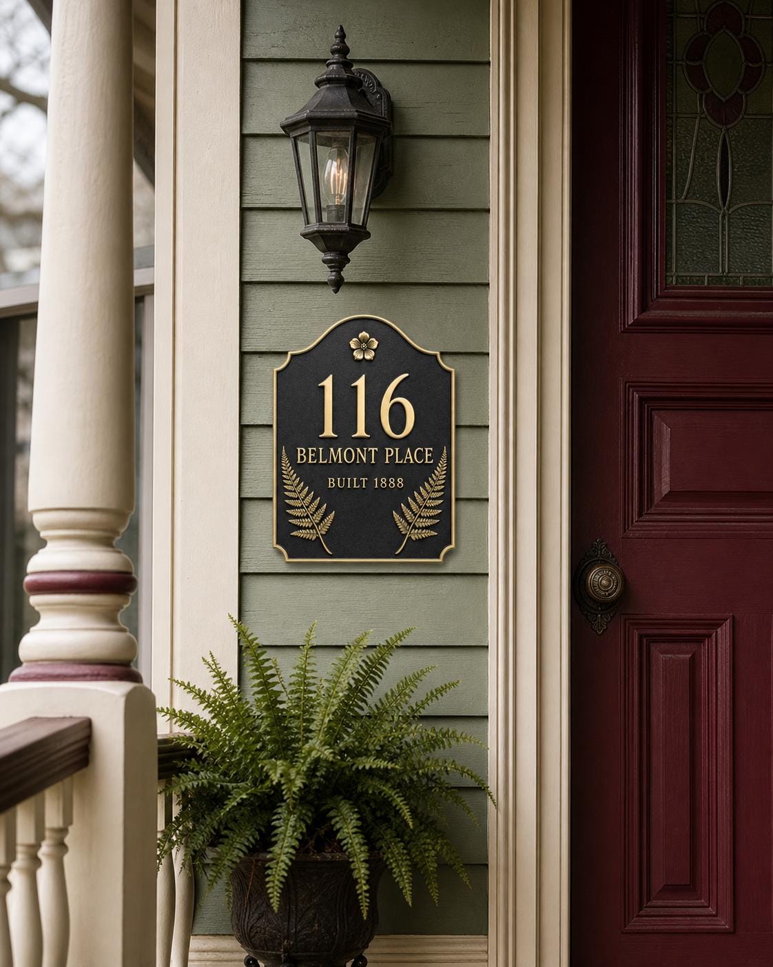 Fern plaque on green siding beside a red front door and a potted fern