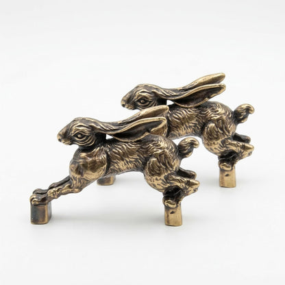 Side view of two antique brass hare handles, one behind the other