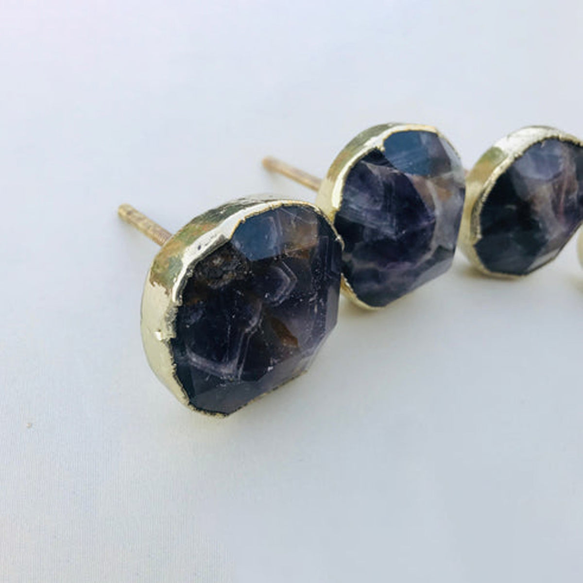 Faceted amethyst knobs in gold bezels, seen at an angle with their bolts