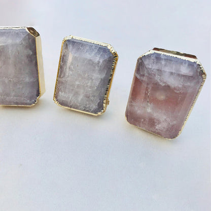Close-up of emerald-cut quartz knobs, milky with a pink tint at the base, in gold bezels