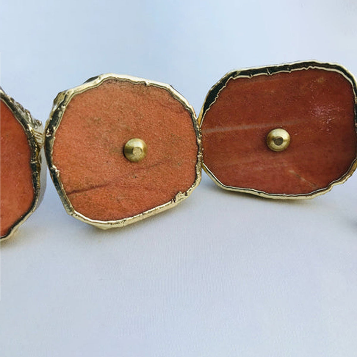 Close-up of burnt orange agate slice knobs with gold rims and brass pins