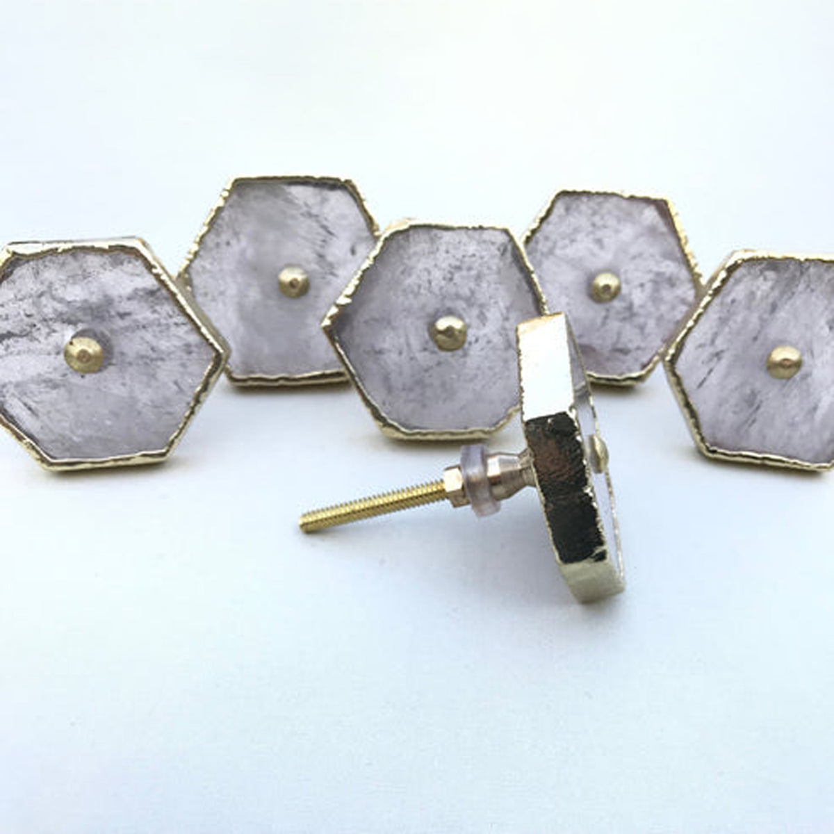 Five hexagonal clear quartz cabinet knobs with gold edges, one turned to show its bolt
