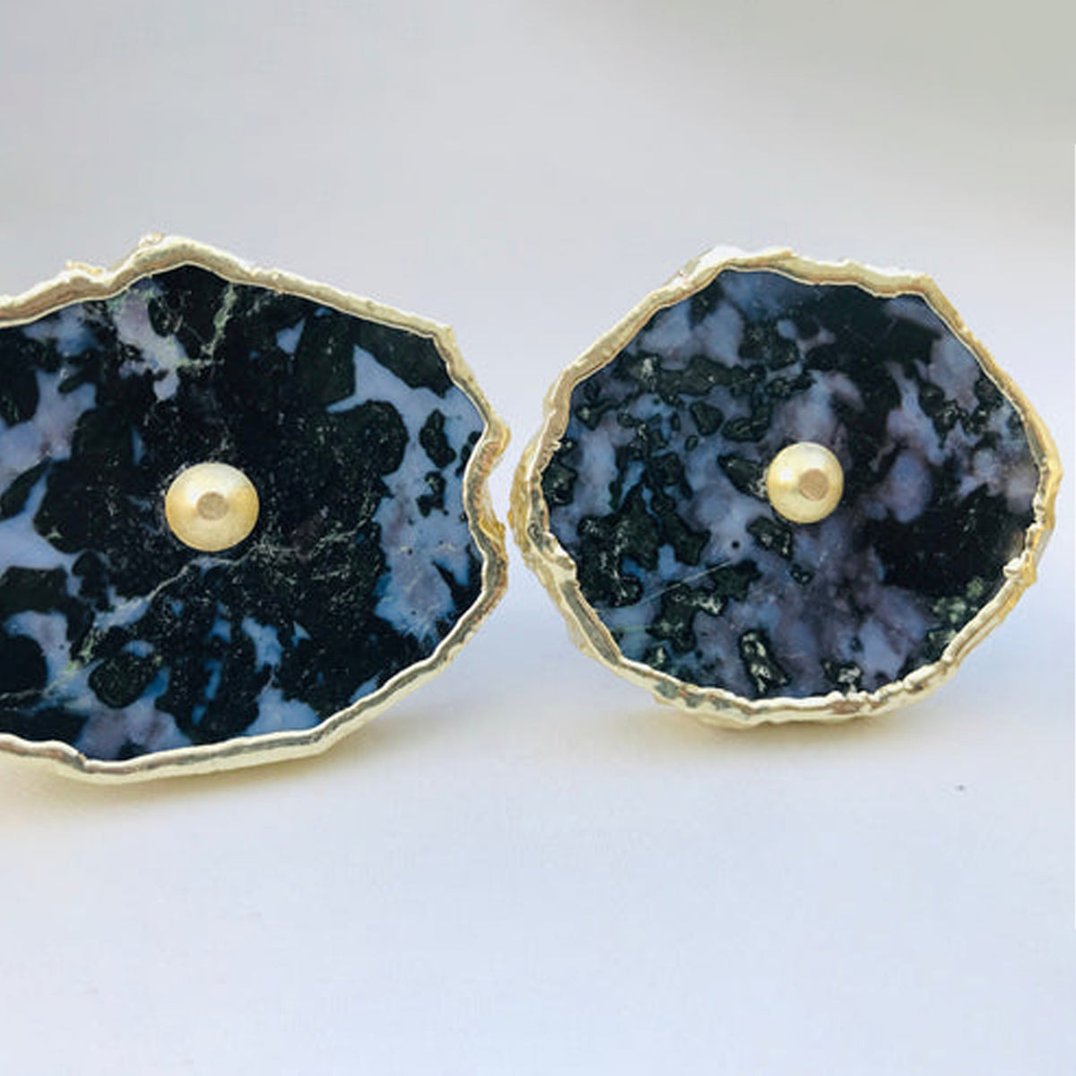 Two dark speckled gabbro slice cabinet knobs with gilded rims