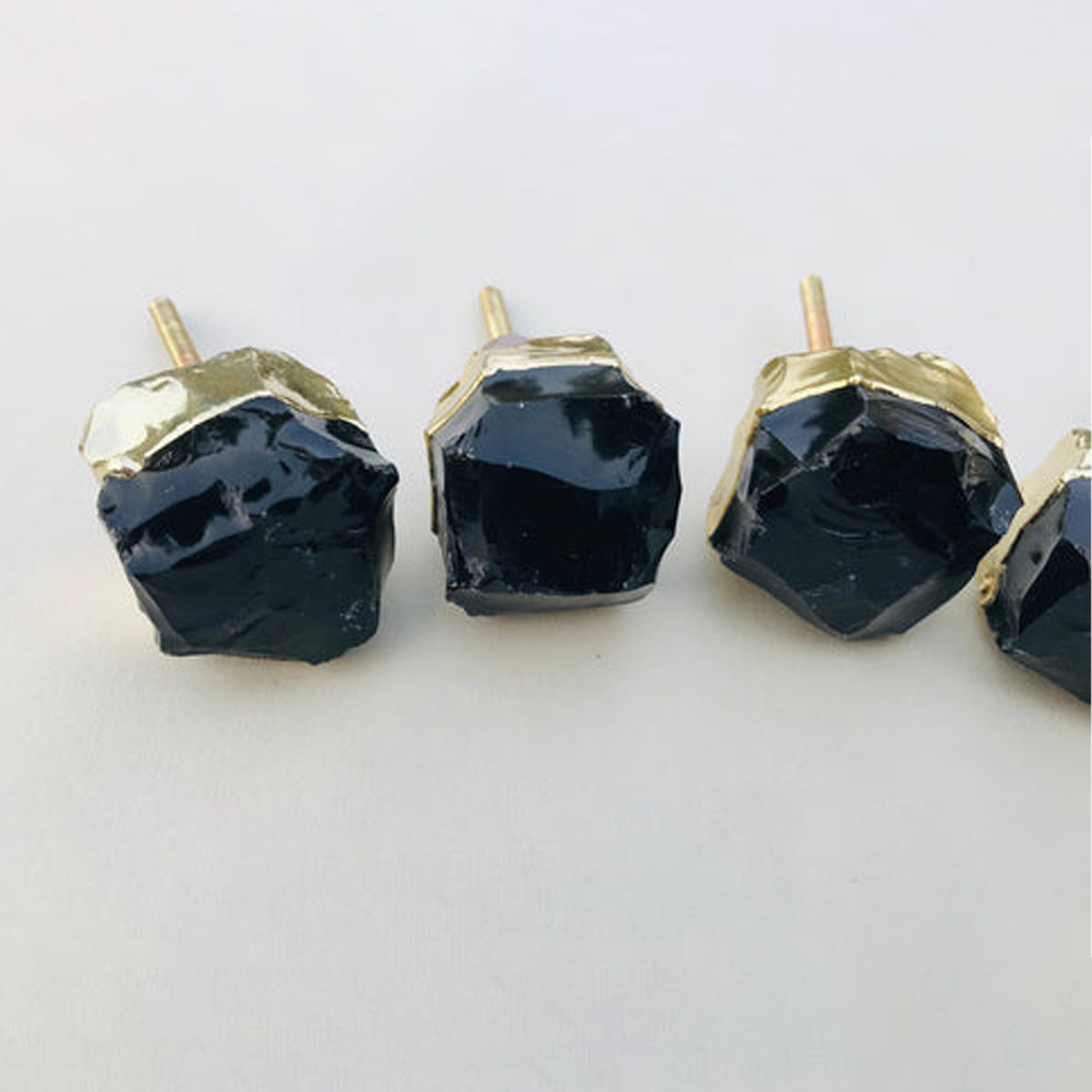 Row of raw black obsidian knobs with gold collars and their bolts
