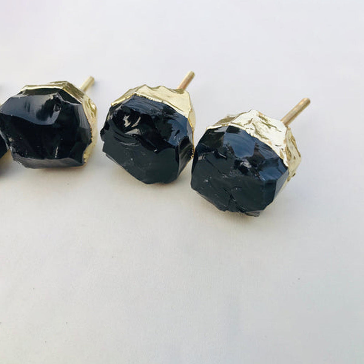 Three raw black obsidian knobs up close, glossy rough faces and gold caps