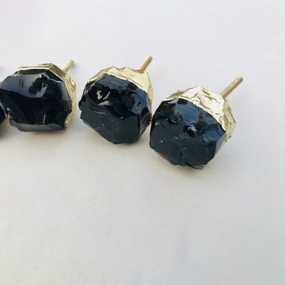 Three raw black obsidian knobs up close, glossy rough faces and gold caps