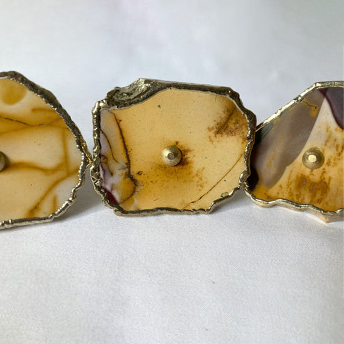 Close-up of a mookaite slice knob in ochre and cream with a brass center pin