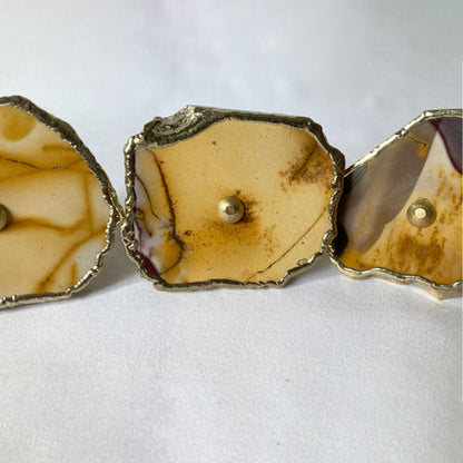 Close-up of a mookaite slice knob in ochre and cream with a brass center pin