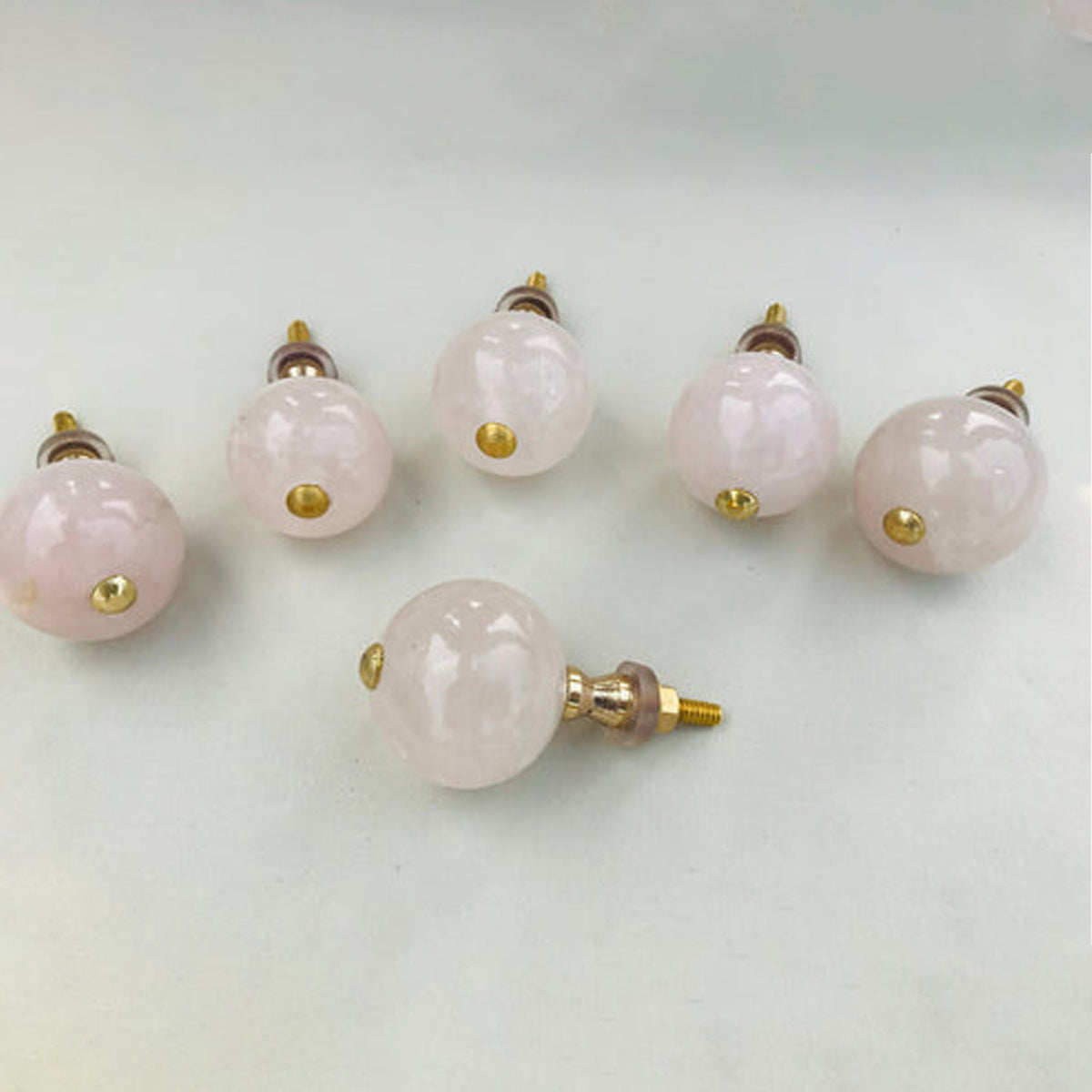 Polished rose quartz sphere cabinet knobs with gold studs, one turned to show its bolt