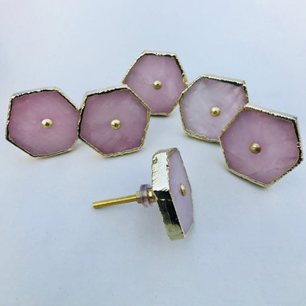 Five hexagonal rose quartz cabinet knobs with gold edges, one turned to show its bolt