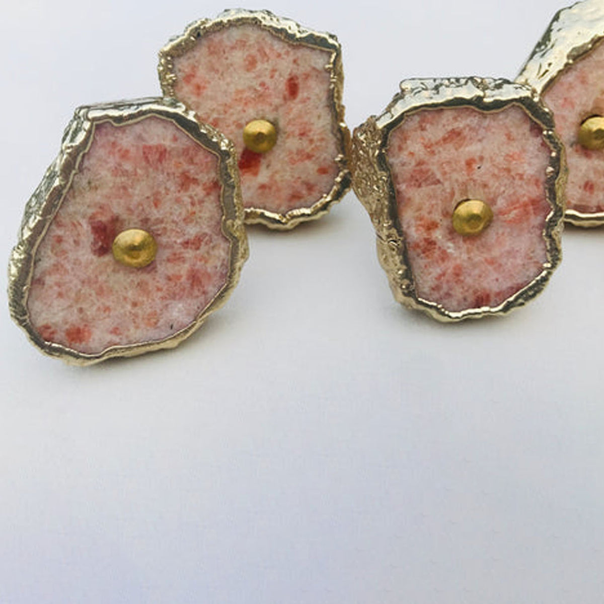 Four sunstone slice knobs, pale pink flecked with red, with gold rims