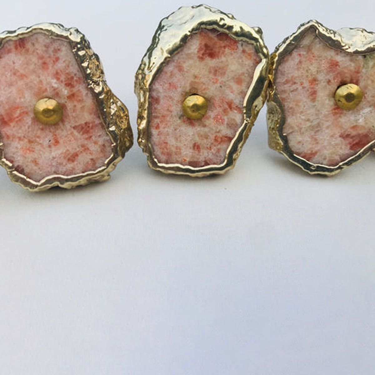 Three sunstone slice knobs in a row, red flecks on a pale pink ground