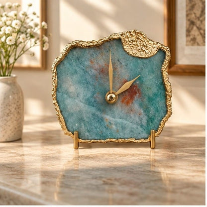 Gray green aventurine desk clock on a marble counter with a vase of white flowers