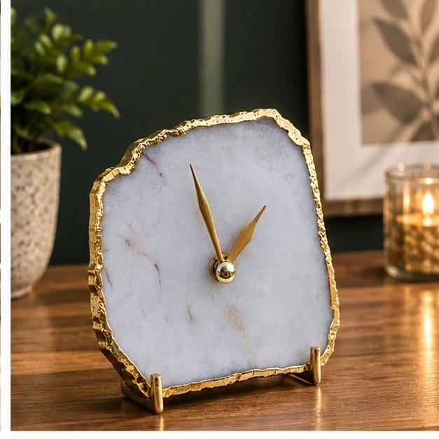 White agate desk clock on a wooden table with a candle and a plant