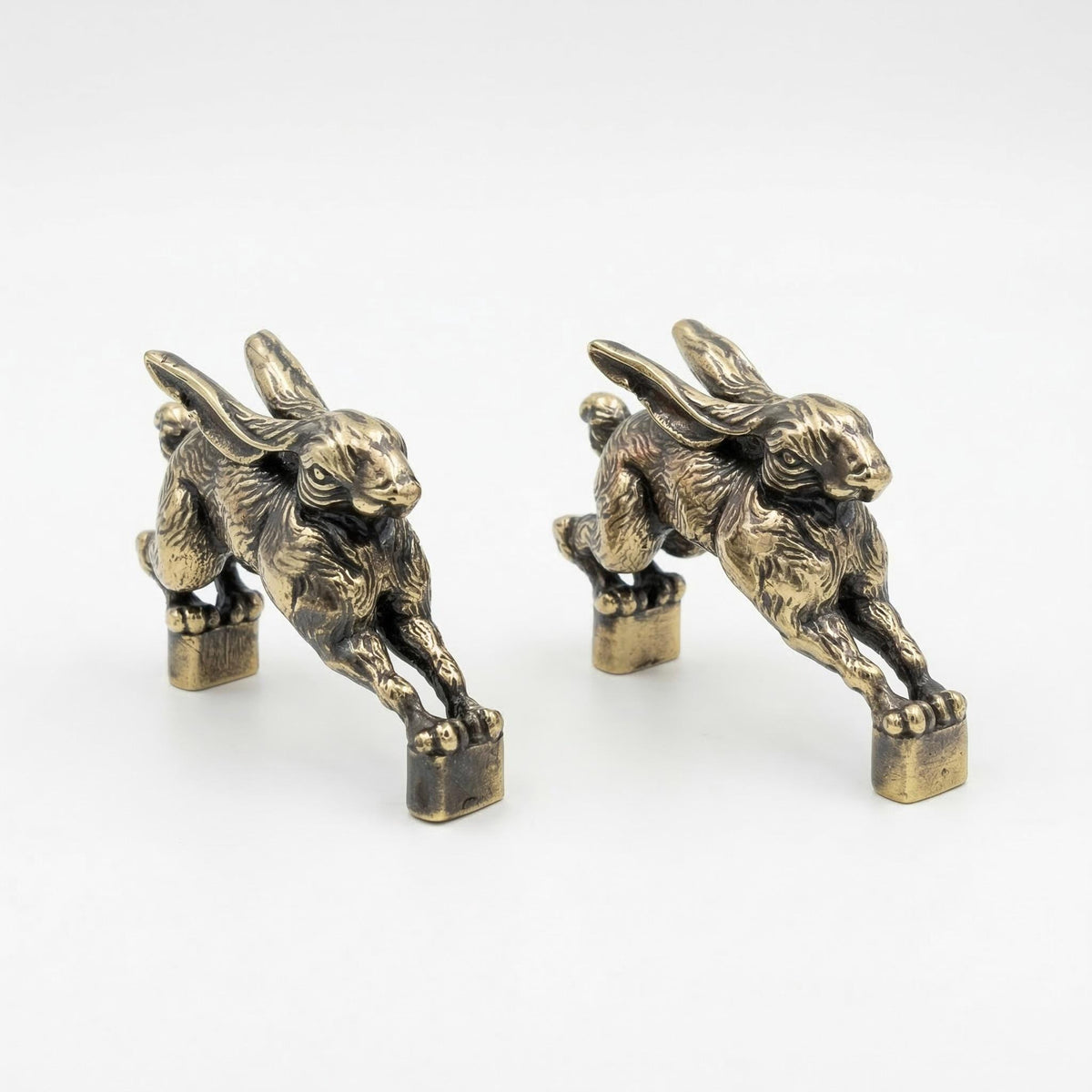 Two antique brass hare handles from the front, showing their faces and posts