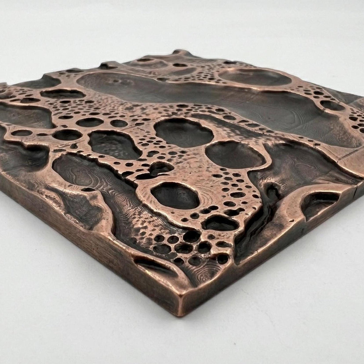 A cosmic crater tile in antique copper at a low angle, showing its edge